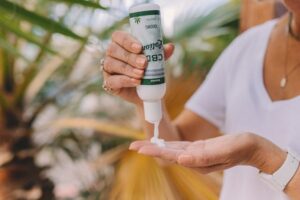 Woman dispensing CBD lotion from a pump bottle into her hand outdoors near tropical plants.