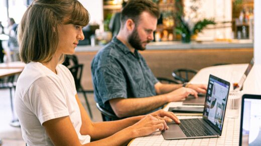 Two professionals working on laptops at a café bar counter, focused on their screens in a modern workspace.