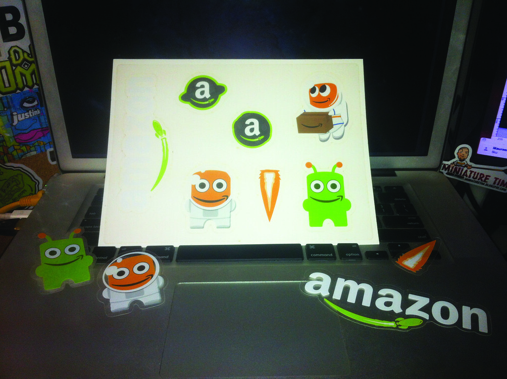 Amazon logo stickers and cartoon mascot decals stuck on a laptop